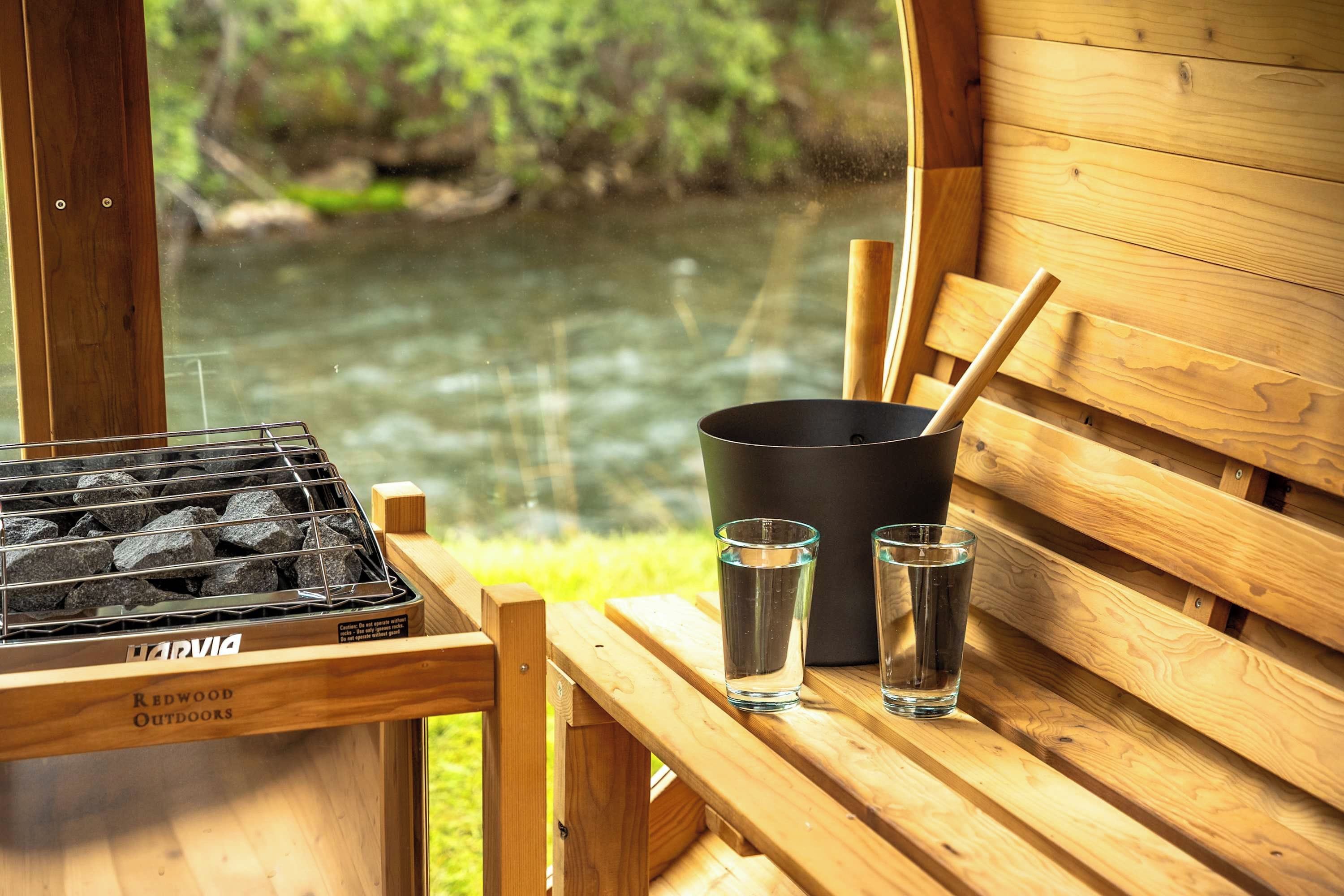 Un banc en bois avec un barbecue et deux verres d’eau, donnant sur une étendue d’eau.
