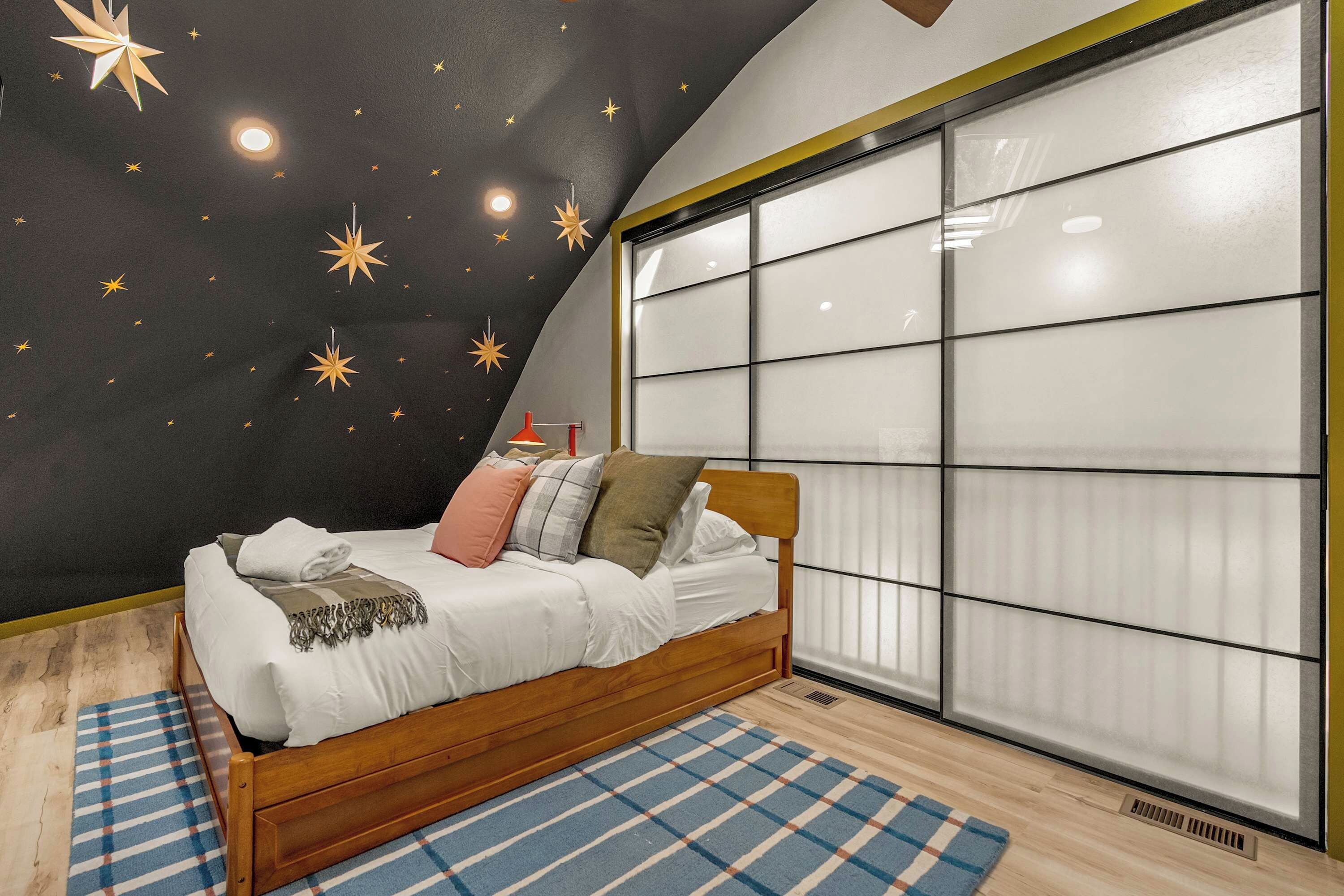 A bedroom with a star-patterned wall, a large window, and a wooden bed.