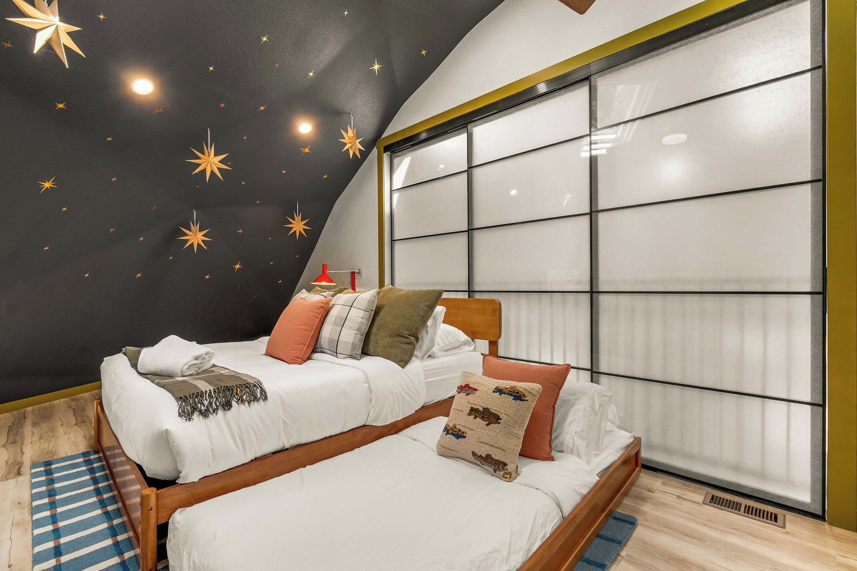 Un dormitorio con techo estrellado, un ventanal grande y una cama con muchas almohadas.