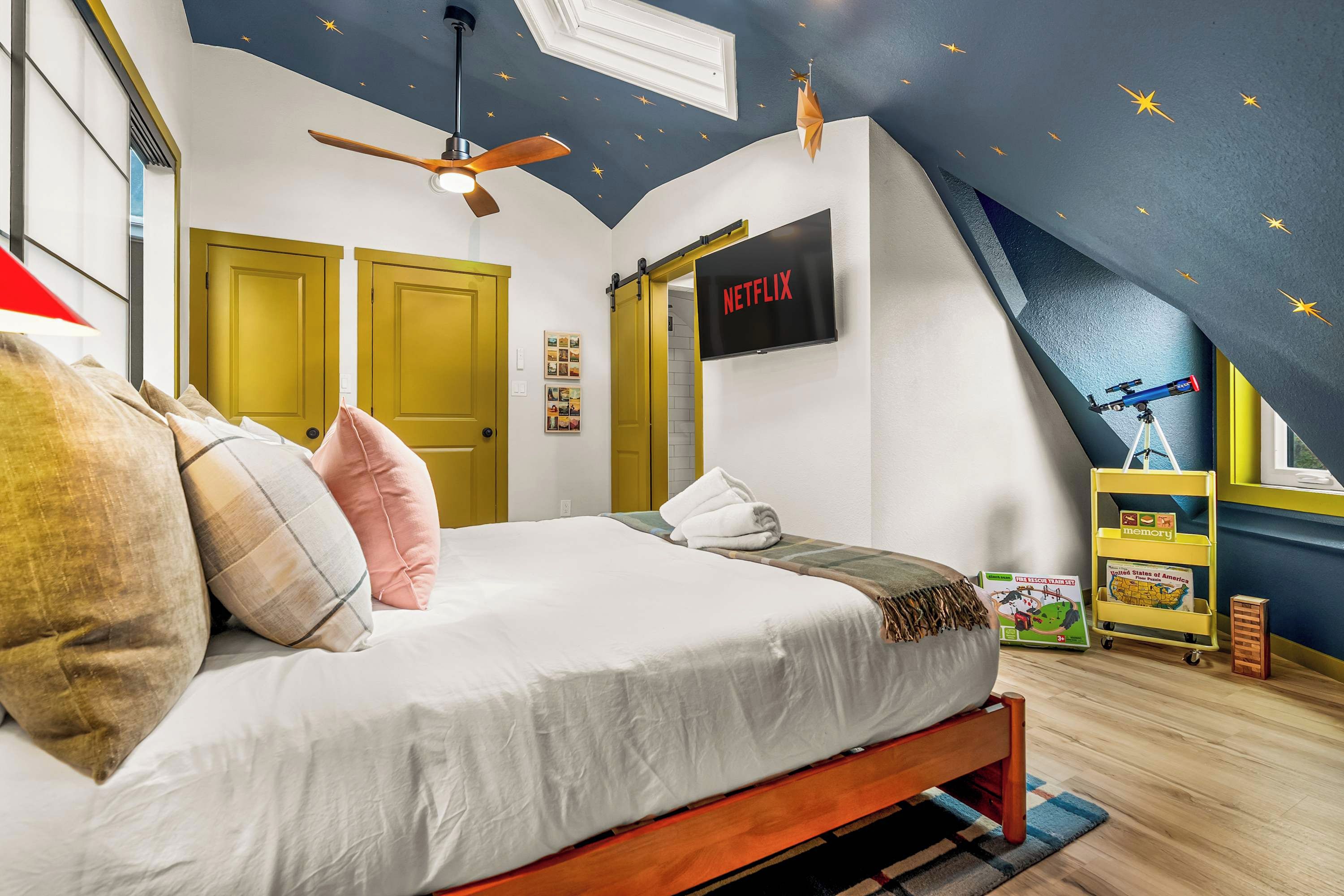 Un dormitorio con cama, ventilador de techo, televisor montado y un telescopio.