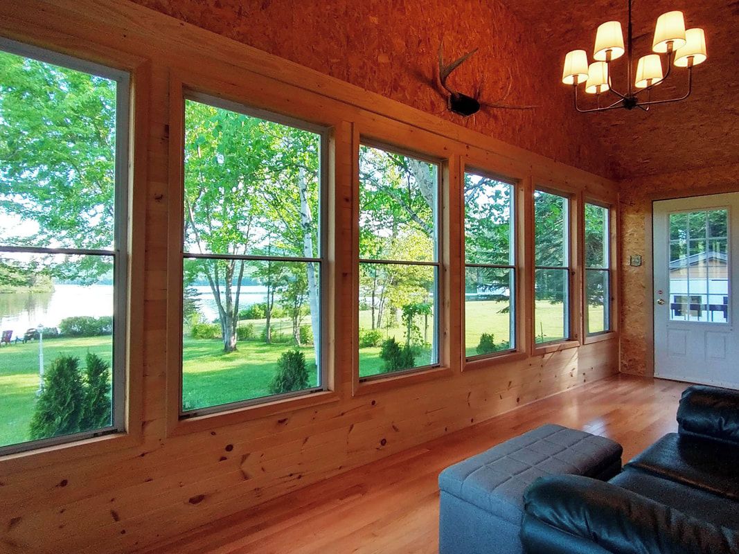 Ein Zimmer mit großen Fenstern, einer Holzbalkendecke und einem schwarzen Ledersofa.