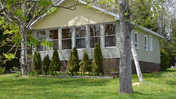 A single-story house with a gabled roof, surrounded by a well-maintained lawn and several evergreen trees.