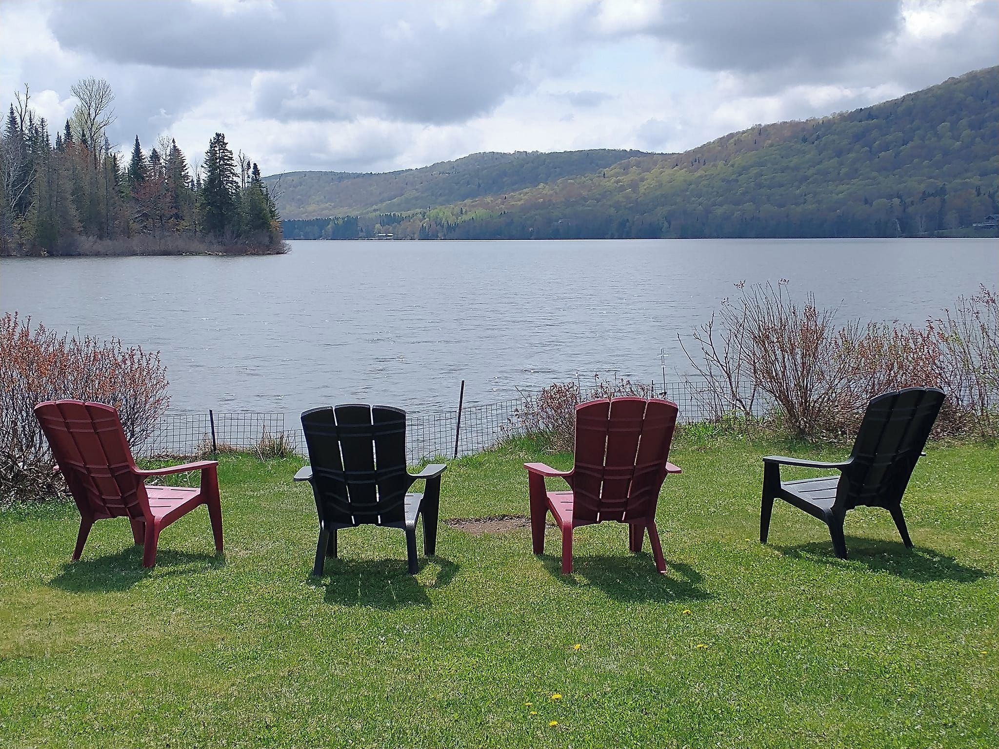 Trois chaises Adirondack sont disposées face à un lac, avec une colline boisée en arrière-plan.