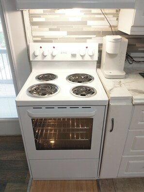 A white kitchen with a four-burner stove, an oven, and a coffee maker on the countertop.