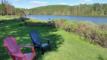 Vista al lago con dos sillas Adirondack sobre un césped.