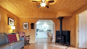 Ein Holzinnenraum mit einer Couch, einem Kamin und einer Küche im Hintergrund.