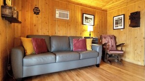Ein Zimmer mit Holzwänden, einem grauen Sofa, einem Holzstuhl und einer Lampe.