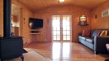 En inredning med träpanel, en svart kamin, en tv på en hylla, en soffa och en takfläkt.