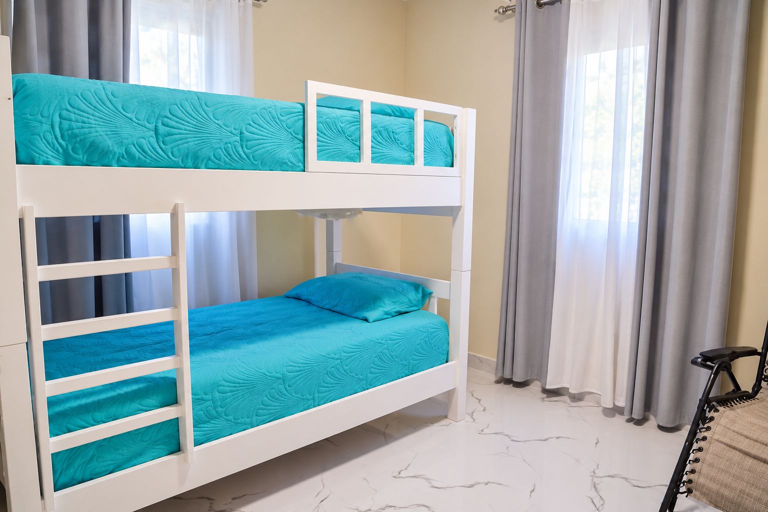 Ein Etagenbett mit blauer Matratze und weißem Gestell in einem Raum mit Marmorboden.