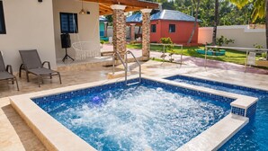 Ein Whirlpool mit einer gefliesten Kante, umgeben von einer Terrasse mit Stühlen und einem kleinen Pool.