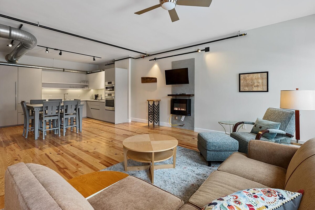 A modern living room with a fireplace, a dining area, and a kitchen.