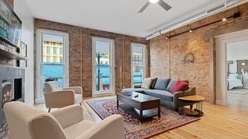 A modern living room with a fireplace, a sofa, a coffee table, and a view through large windows.