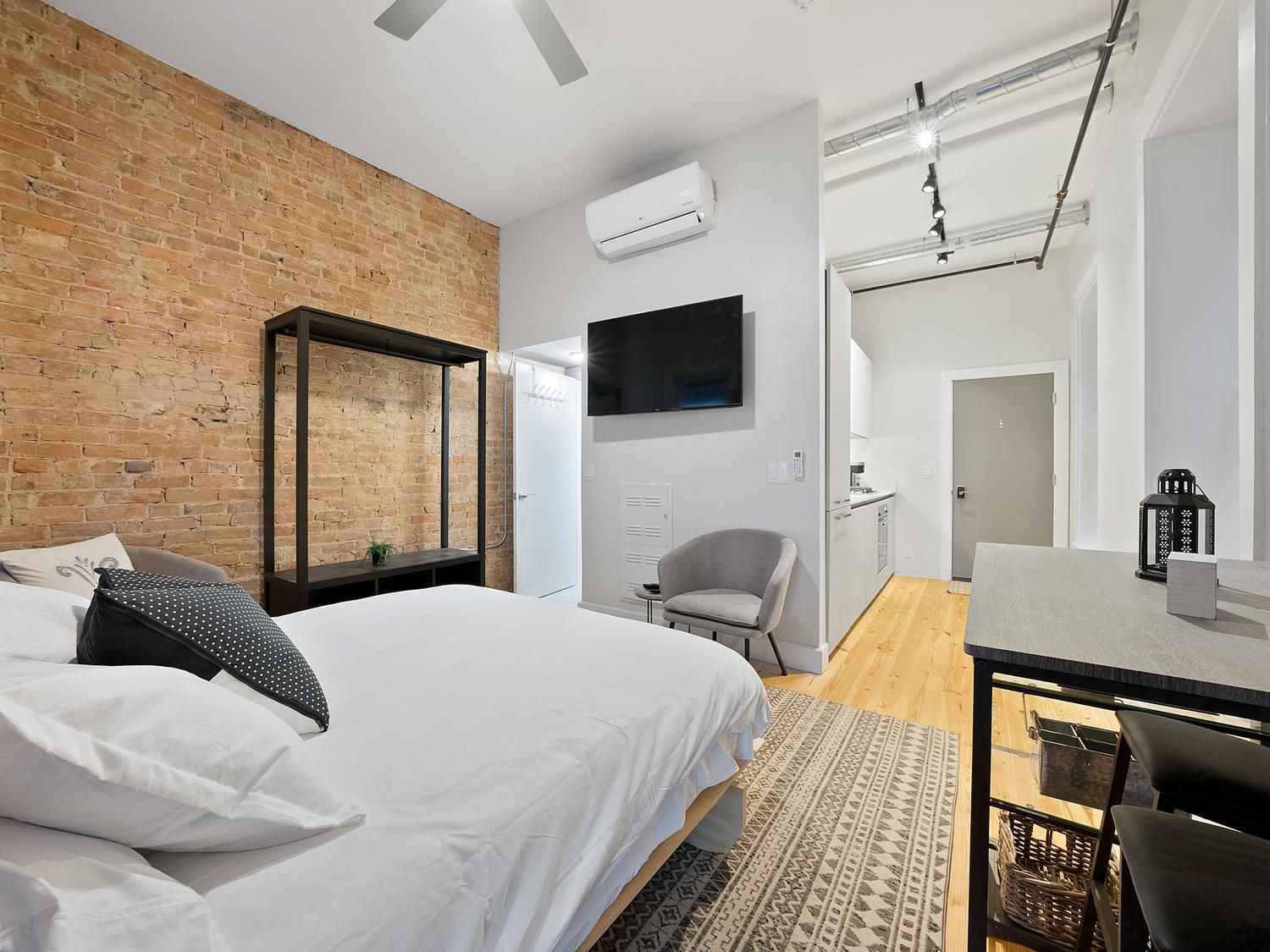 A modern bedroom with a brick wall, a bed with white bedding, a desk with a chair, and a television.