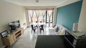 Ein Wohnzimmer mit einer Couch, einem Esstisch mit Stühlen, einem Fernseher und einer Mikrowelle.