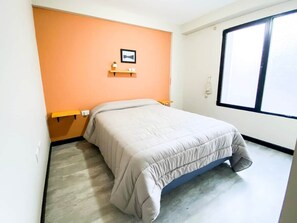 Ein Schlafzimmer mit einem Bett, einem Fenster und einem an der Wand befestigten Regal.