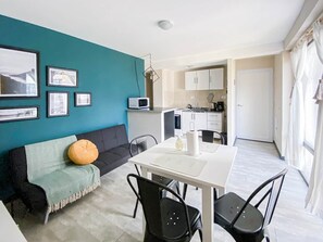 Una sala de estar moderna con una pared de acento color turquesa, un sofá negro, un cojín naranja redondo y una zona de comedor con una mesa blanca y sillas negras.
