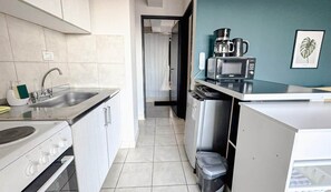 Une cuisine de taille réduite, équipée d’un évier, d’une cuisinière, d’un four à micro-ondes et d’une petite poubelle.