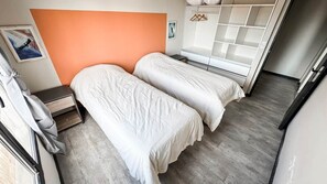 Een slaapkamer met twee bedden, een kledingkast, een nachtkastje en een raam.