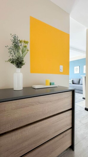 Een modern interieur met een houten kast, een witte vaas met bloemen en een heldergele wand.