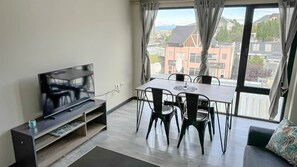A modern living room with a flat-screen TV on a stand, a dining table with chairs, and a large window with curtains. - Amanecer del Fuego VI (Ushuaia)