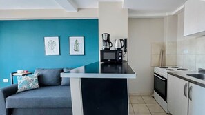 Een knus woongedeelte met een kitchenette, een bank en twee ingelijste foto’s aan de muur.