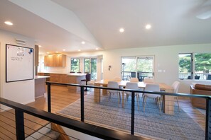 A modern kitchen with wooden cabinets, a dining area with a large table and chairs, and a view of trees through the windows. - 4BR Eagle River Chain Lakefront | Walk Downtown (Eagle River)