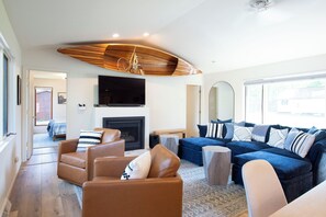 A modern living room with a fireplace, leather sofas, a television, and a large window. - 4BR Eagle River Chain Lakefront | Walk Downtown (Eagle River)