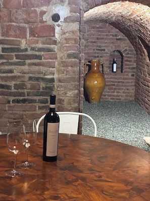 Ein Tisch mit einer Weinflasche und zwei Gläsern, eine Ziegelwand und eine große Vase.