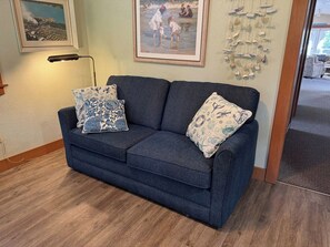 Un canapé bleu foncé agrémenté de coussins à motifs, un tableau encadré au-dessus, et un élément décoratif fixé au mur.