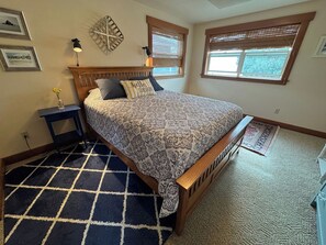 A bedroom with a bed, nightstands, a rug, and a window with blinds. - Juniper Beach Cabin on Camano Island (Camano Island)