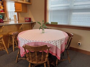 A round dining table with a polka dot tablecloth, surrounded by wooden chairs, in a room with a window and blinds. - Juniper Beach Cabin on Camano Island (Camano Island)