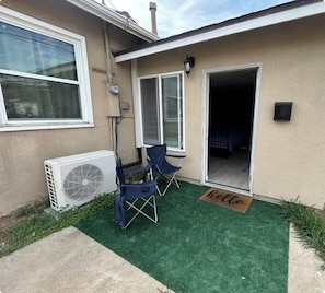 A residential property with a covered patio, two folding chairs, a small air conditioning unit, and a welcome mat. - Private Studio + Parking + Laundry + 15 Min to SD (La Mesa)