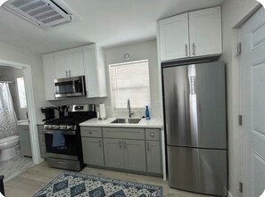 A modern kitchen with stainless steel appliances, white cabinetry, and a patterned rug. - Private Studio + Parking + Laundry + 15 Min to SD (La Mesa)
