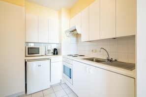 A compact kitchen with white cabinets, a microwave, a coffee maker, a stove, and a sink. - Apartment in Blankenberge With Sea Views (Blankenberge)