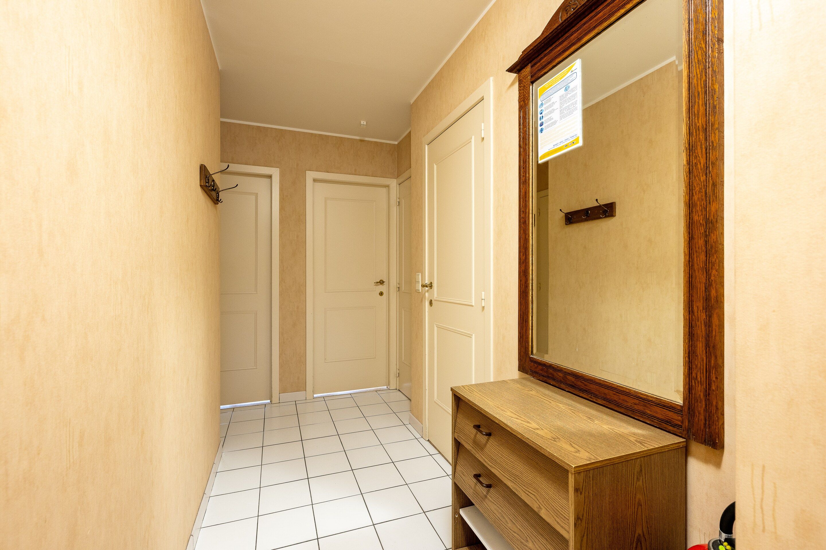 A hallway with two white doors, a wooden vanity with a mirror, and a tiled floor.