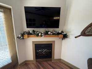 A living room with a flat-screen TV mounted above a fireplace, flanked by wooden shelves with a garland. - Updated Pigeon Forge Condo.  3BDR 2BA W/ 2 Pools on the Parkway (Pigeon Forge)