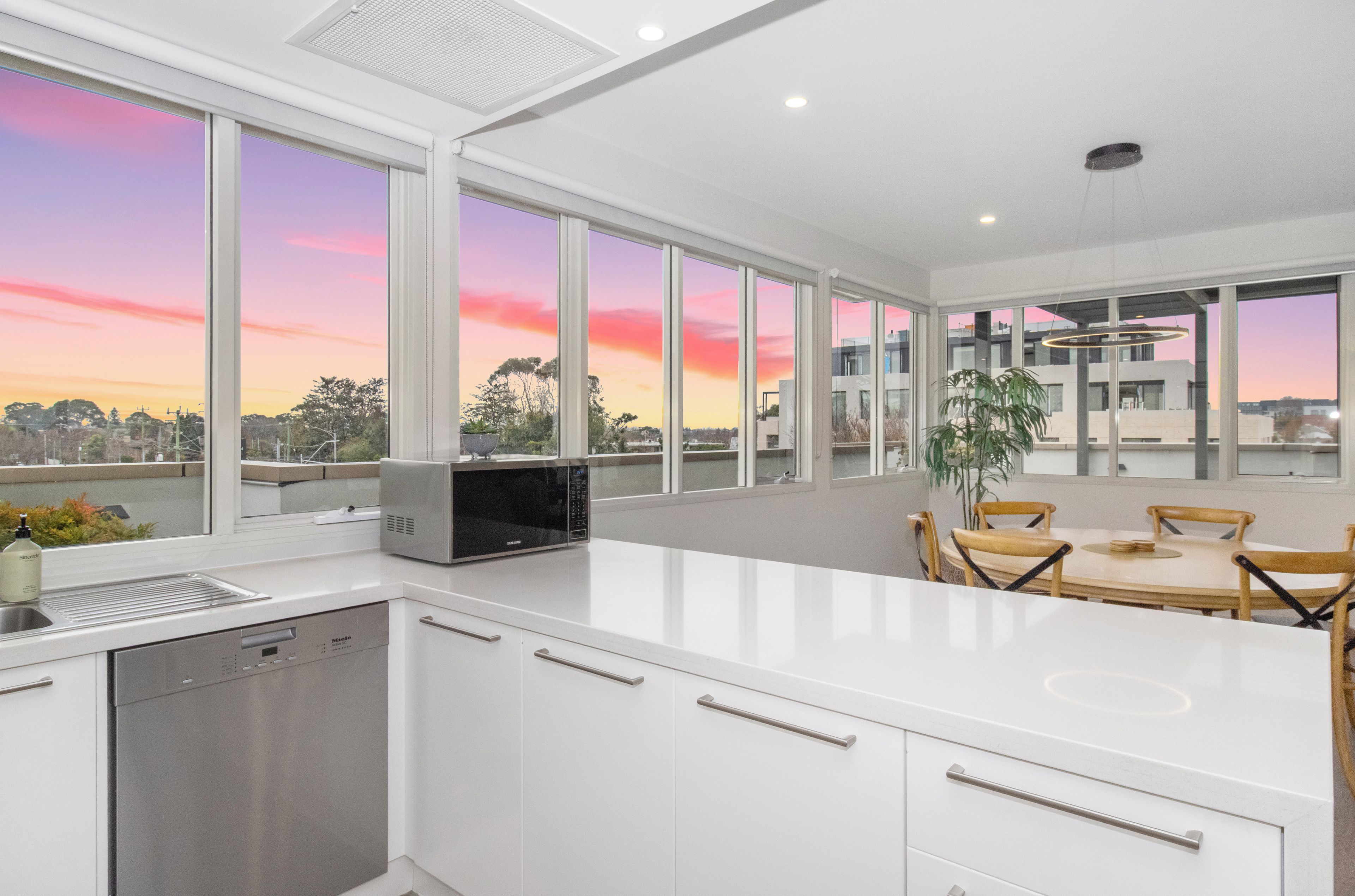 A modern kitchen with a large island, white cabinetry, and a view of the sunset through expansive windows.