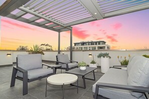 An outdoor seating area with modern furniture, a view of a building, and a sunset sky. - Corner Penthouse with City Views in Armadale (Armadale)