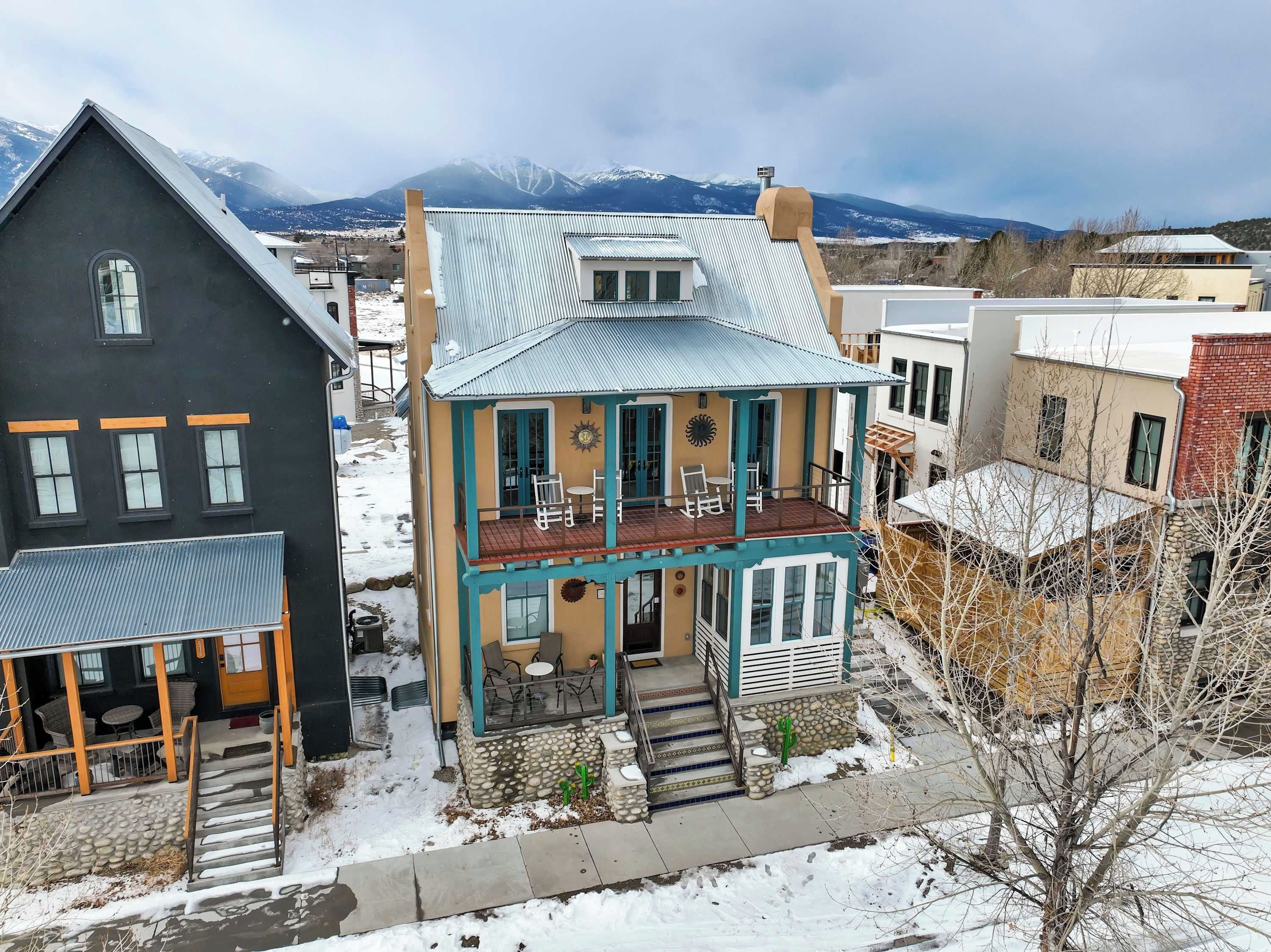 A two-story house with a balcony, a stone foundation, and a view of mountains in the background.