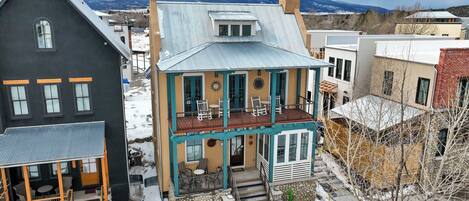 A two-story house with a balcony, a stone foundation, and a view of mountains in the background.
