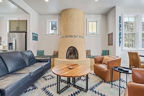 Una sala moderna con chimenea, sofás de cuero, una mesa redonda de madera y una zona de cocina con refrigerador.