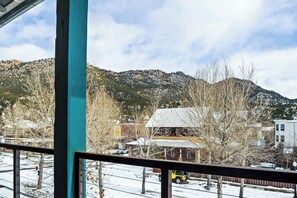 Vista desde una ventana sobre un paisaje nevado con una montaña al fondo, un edificio de techo rojo y árboles sin hojas.