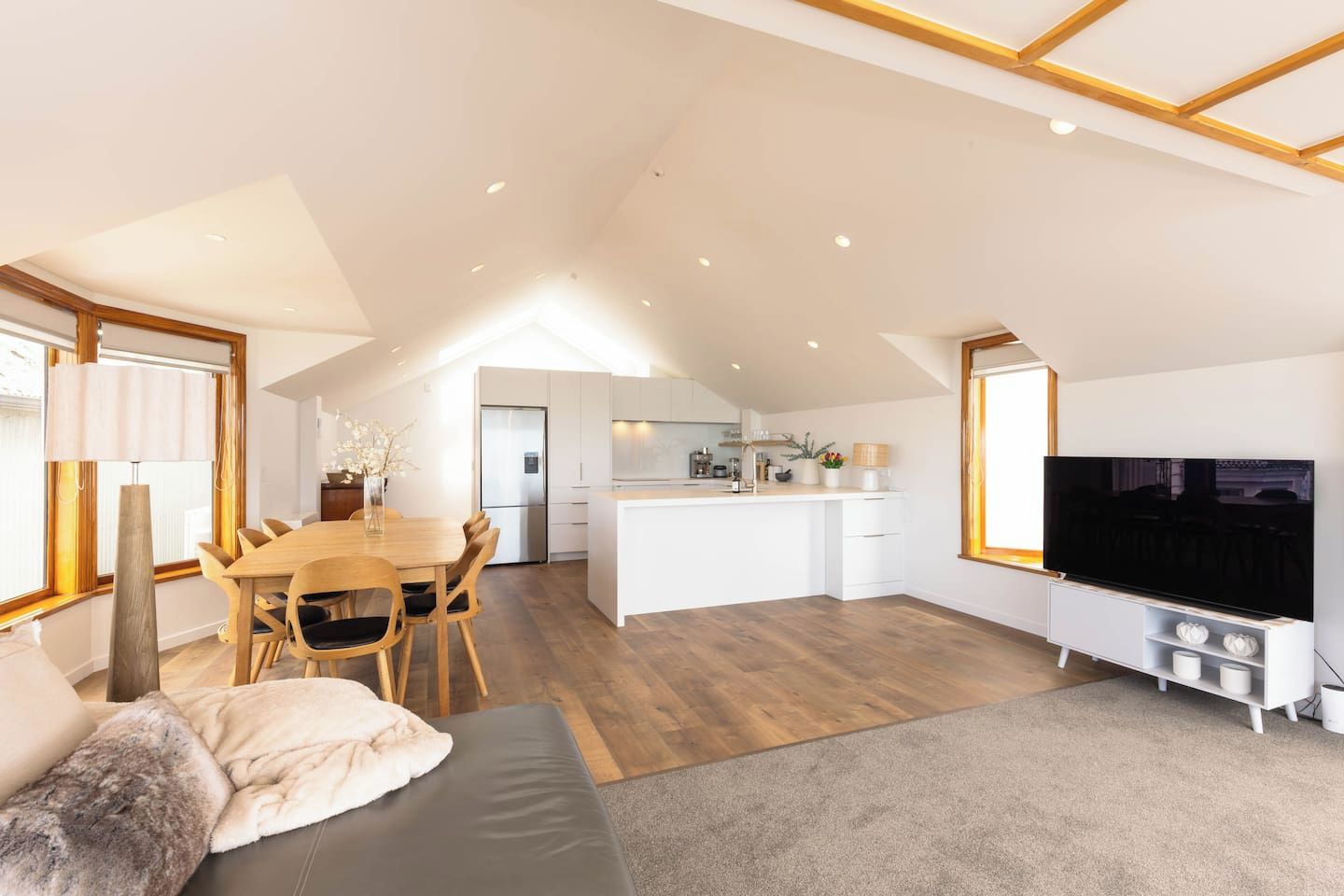 A modern apartment with a dining area, kitchen, living room, and a TV.