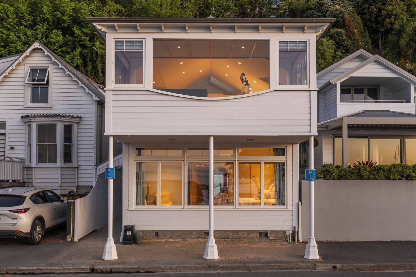 Une maison à deux étages avec un balcon, une voiture garée devant et un panneau de signalisation indiquant un espace de stationnement.