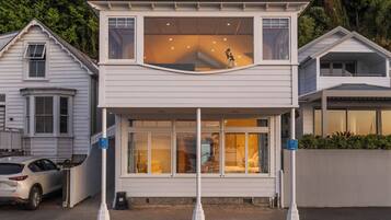 Une maison à deux étages avec un balcon, une voiture garée devant et un panneau de signalisation indiquant un espace de stationnement.