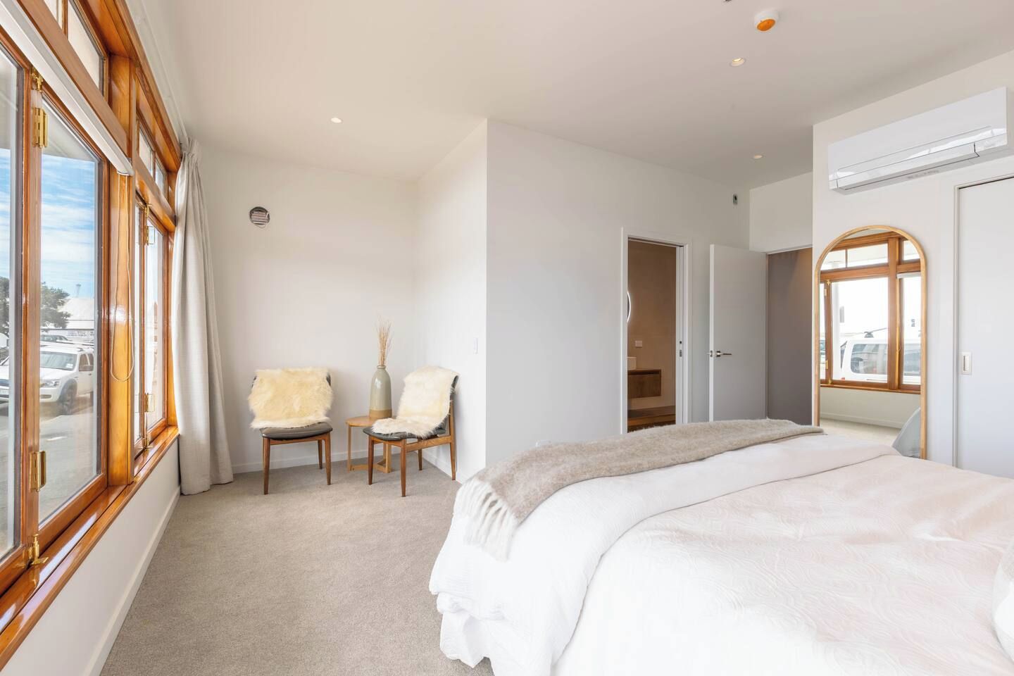 A bedroom with a large bed, two chairs, a wardrobe, and a window with curtains.