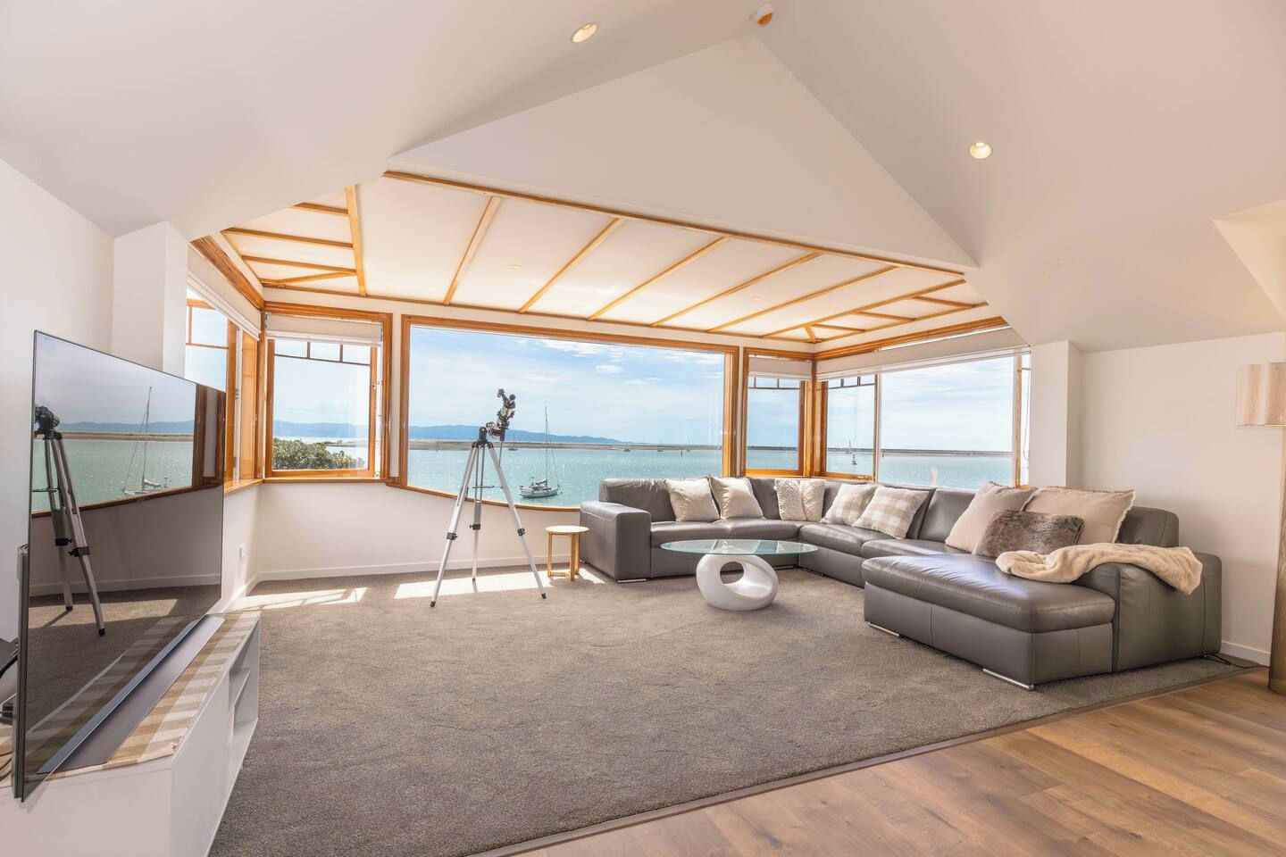 Un salon moderne doté d’un grand canapé d’angle, d’un téléviseur à écran plat, d’un télescope et offrant une vue sur la mer grâce à de grandes fenêtres.