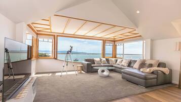 Un salon moderne doté d’un grand canapé d’angle, d’un téléviseur à écran plat, d’un télescope et offrant une vue sur la mer grâce à de grandes fenêtres.