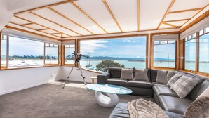 Ein modernes Wohnzimmer mit einem großen Fenster, das Meer und Berge zeigt.