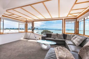 Un salón moderno con un ventanal grande que ofrece vistas al mar y a las montañas.